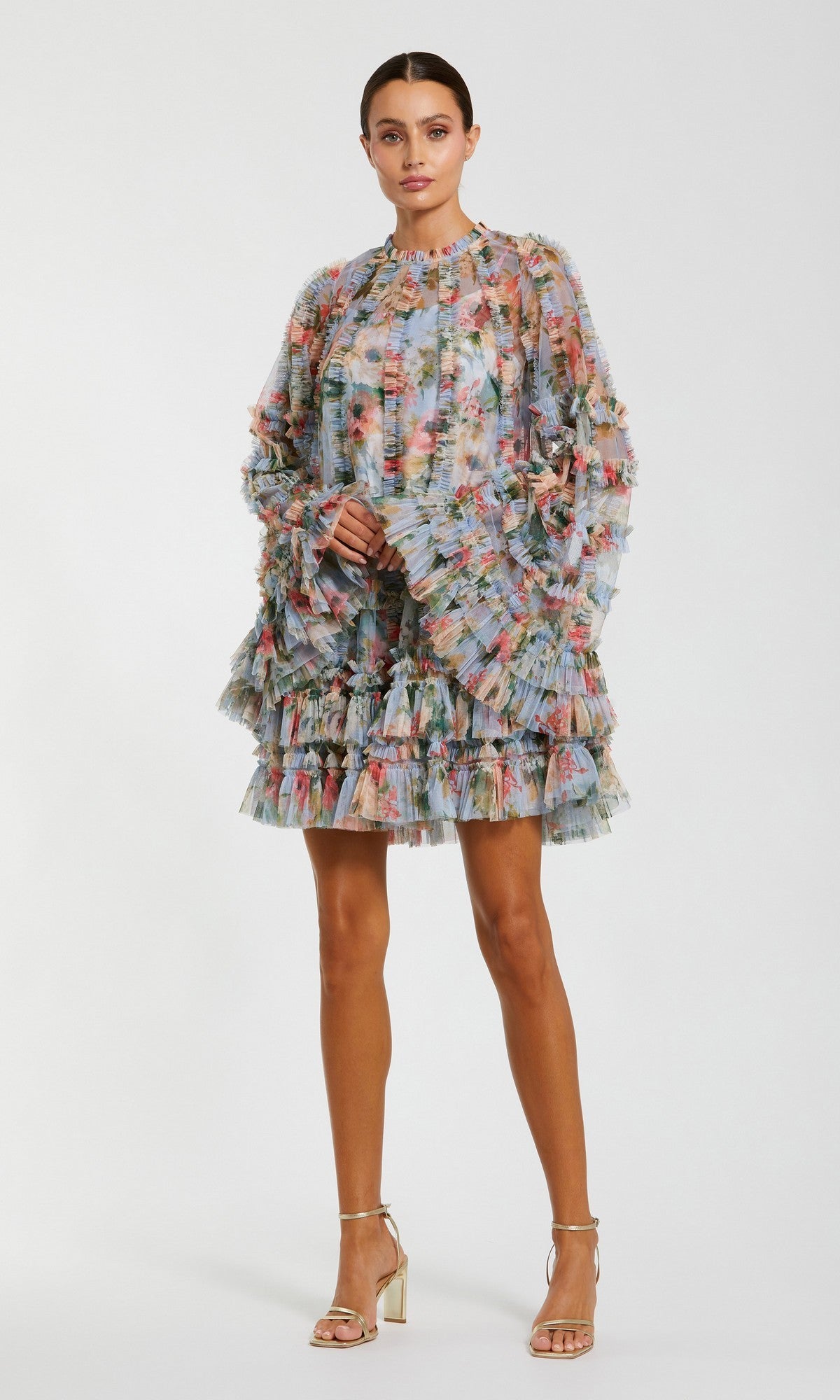 A woman wears the Mac Duggal 8300 Bell-Sleeve Floral Wedding Guest Dress, featuring sheer layers and ruffles, paired with metallic heels—a chic pick for a short wedding guest dress.